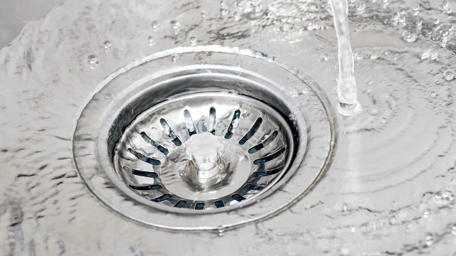 Water pooling around a stainless steel sink drain strainer while the faucet runs