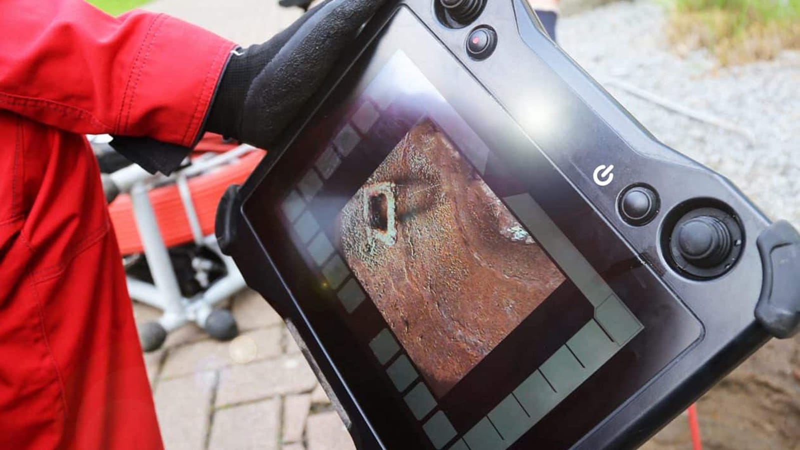 Plumber holding a sewer camera monitor that shows the inside of a damaged pipe