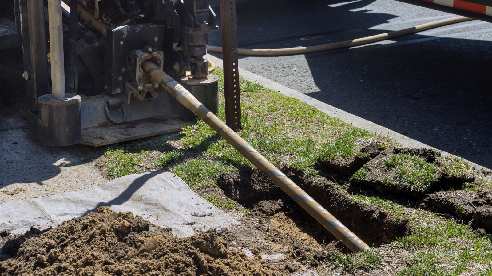Boring rig feeding pipe into a shallow trench along a lawn to install a new sewer line