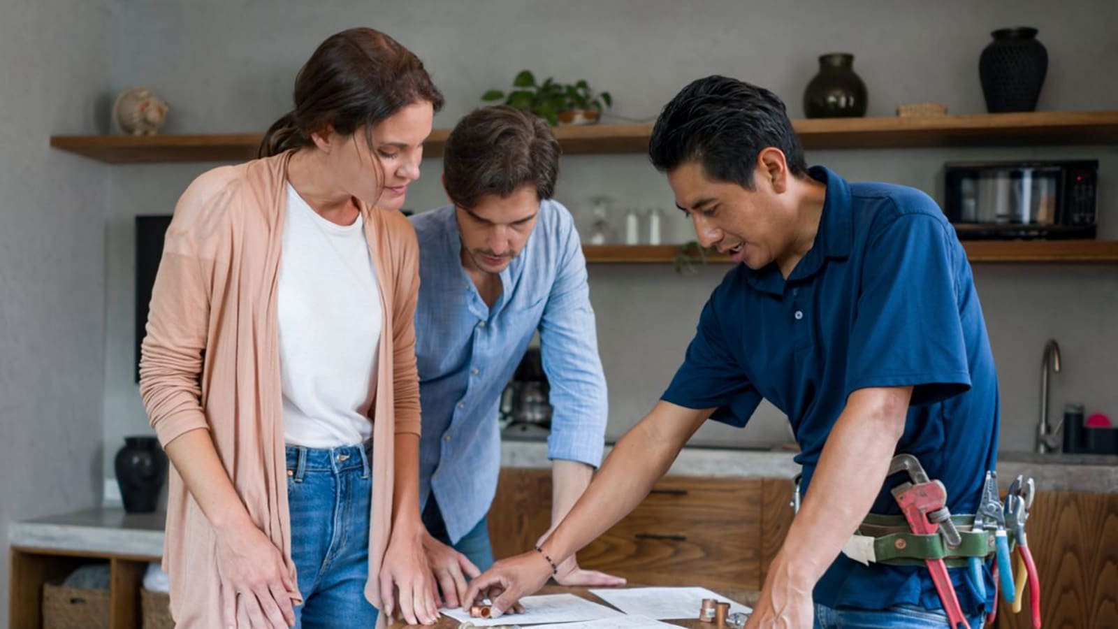 Plumber reviewing project plans with two homeowners at a kitchen counter